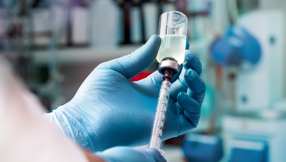 a gloved hand pulling liquid out a bottle into a syringe